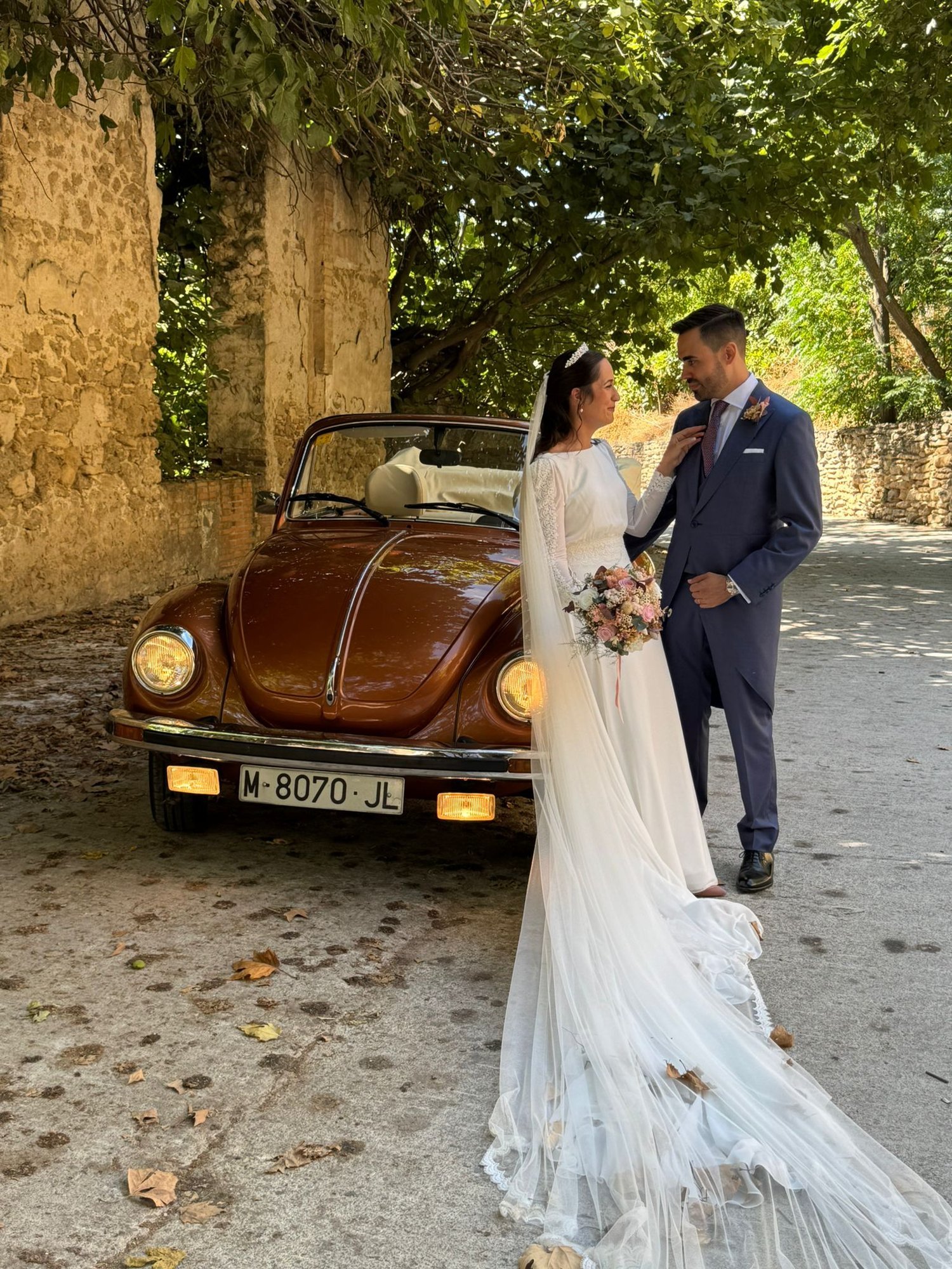 La novia ajusta la corbata del novio junto al coche clásico